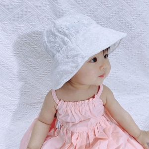 Una bambina asiatica seduta con un vestito rosa e un berretto bianco che guarda verso destra