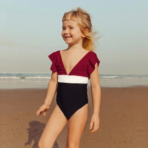 Ragazza bionda sorridente sulla spiaggia che indossa un costume da bagno intero