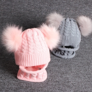 due cappelli con pompon e sciarpa integrata, uno rosa sul davanti e l'altro grigio sul retro a destra, montati su tessuto grigio