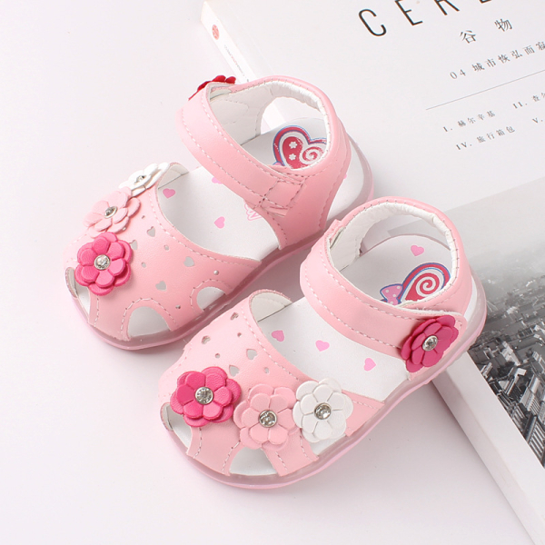 Sandalo rosa per ragazze con 4 piccoli fiori di colori diversi, posizionati su una rivista e un tavolo bianco