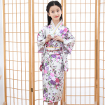 davanti a uno schermo giapponese, una bambina indossa un kimono tradizionale bianco con un motivo floreale rosa