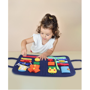 Bambina su un tavolo che cerca di aprire la zip sulla lavagna didattica con diversi oggetti come un bottone, un bottone a pressione, un cordoncino, una clip, una cintura, ecc