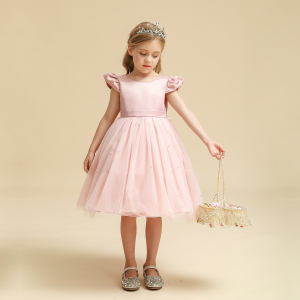 Una bambina in piedi con un abito di tulle rosa, lo sfondo è beige