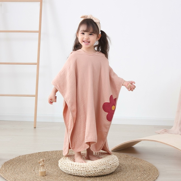 Abbigliamento da spiaggia per ragazze sotto forma di un poncho rosa con un fiore rosso, indossato da una ragazza in piedi su un cuscino bianco