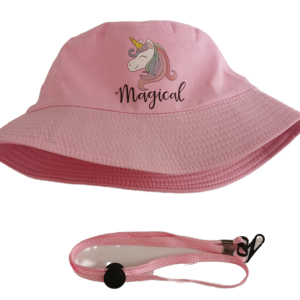 Su sfondo bianco, un cappello con pompon rosa chiaro con l'illustrazione di un unicorno bianco con criniera multicolore e corno dorato e la scritta Magical sul davanti e un cordoncino di tenuta laterale con un bottone di chiusura in plastica nera e ganci in plastica nera.