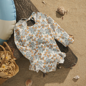 Costume da bagno a maniche lunghe da ragazza, stampato, appoggiato su un pezzo di legno su una spiaggia, con elementi intorno a esso