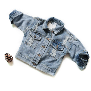 Giacca di jeans blu strappata, appoggiata su uno sfondo bianco, con una pigna accanto