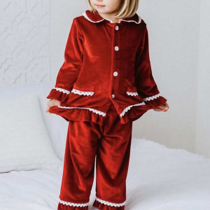 Una bambina bionda in piedi, con un pigiama natalizio di velluto rosso