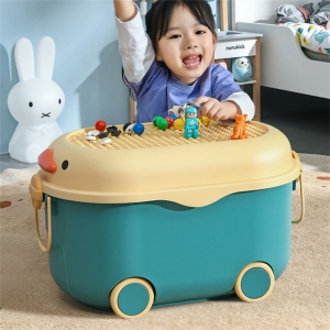 Una bambina bruna in una camera da letto appoggiata a una scatola di giocattoli con ruote