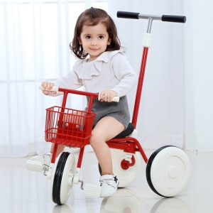Bambina marrone seduta su un triciclo rosso in una stanza vicino a una finestra