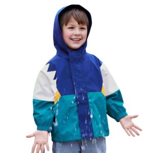 Un bambino caucasico che indossa un sottile parka patchwork con cappuccio verde, blu, bianco e giallo su uno sfondo semplice