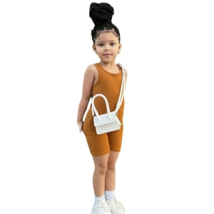 Una ragazzina bruna con trecce e uno chignon che indossa una pettorina marrone a coste e una borsa a tracolla bianca