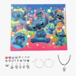 Calendario dell'Avvento Stitch gioielli da creare su sfondo bianco. La scatola nei colori di Stitch in alto e sotto, i charm, due braccialetti in metallo e una collana con cordoncino nero.